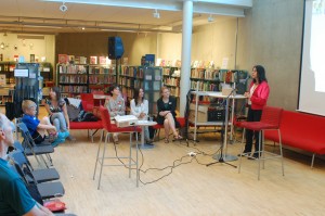 People sitting and watching a woman giving a presentation.