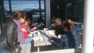 A group of seven project members sitting around a table outside in the sun, drinking coffee and discussing