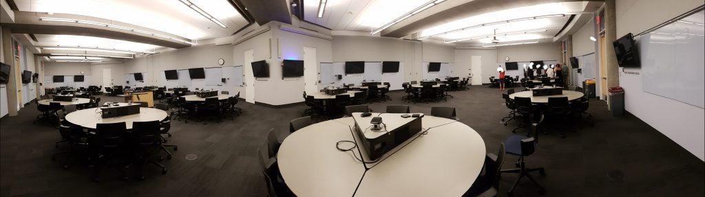 Stort klasserom med mange gruppebord og skjerm