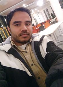 An Indian man with a mustache and very short beard wearing a white and black jacket