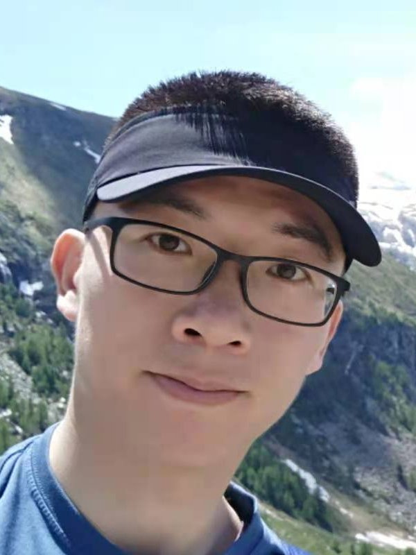 A young Chinese man wearing glasses and a visor in front of a mountain