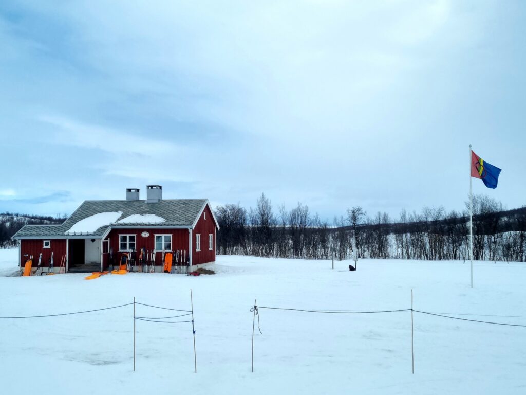 hytte, rødt trebygg, trær i bakgrunn, snødekt bakke, vinterlandskap